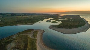 An aerial view of a coastal landscape with a large body of water, a curved shoreline, and a small island with a road leading to it. - Alice House, Burnham Market, Norfolk (Burnham Market)