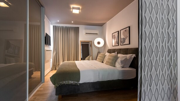 A modern bedroom with a bed, bedside lamp, and a view through a glass door. - Phaedrus Living Luxury Flat Vouliagmeni (Vari-Voula-Vouliagmeni)