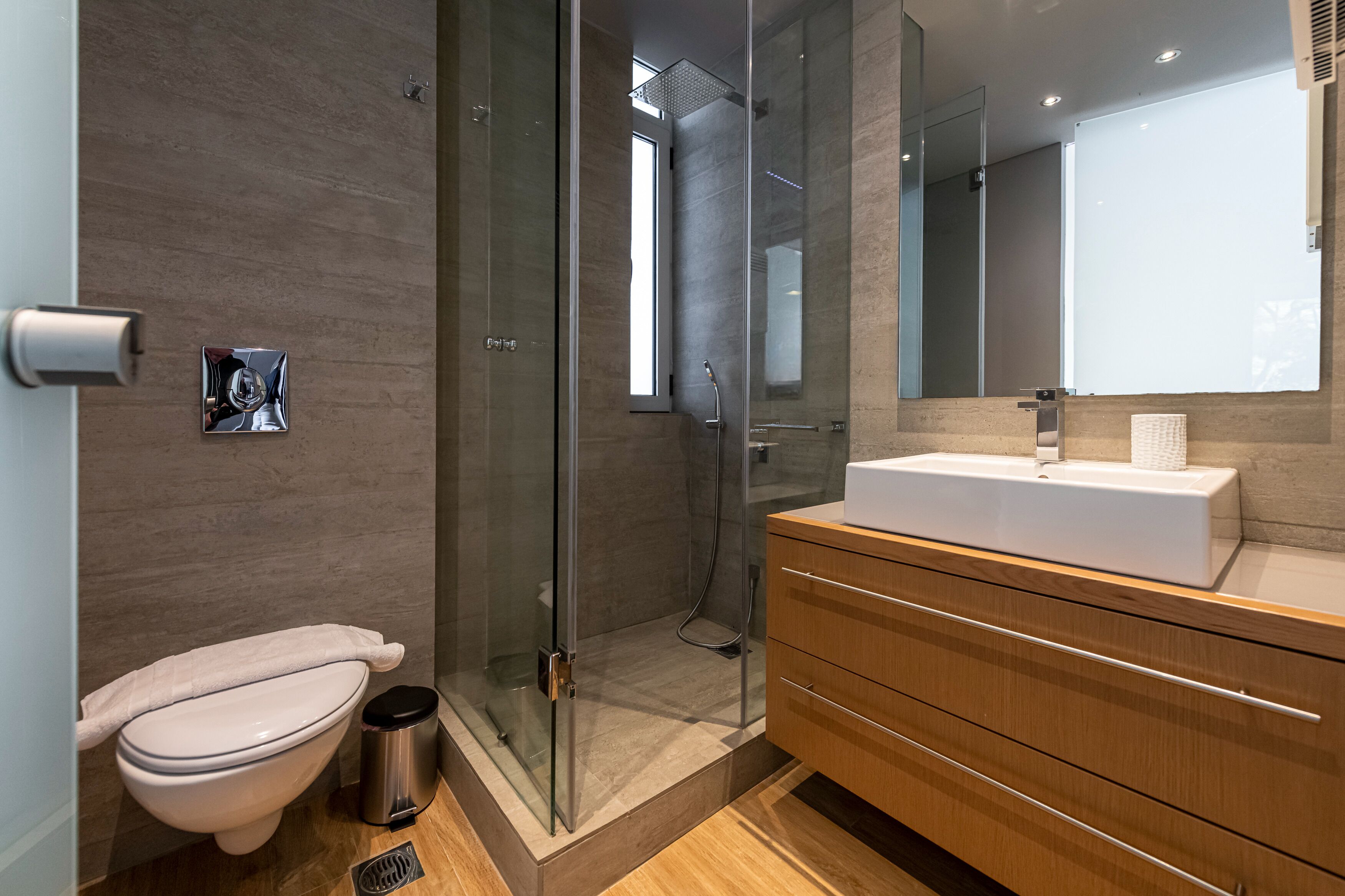 A modern bathroom with a glass-enclosed shower, a white sink, and a wooden vanity.