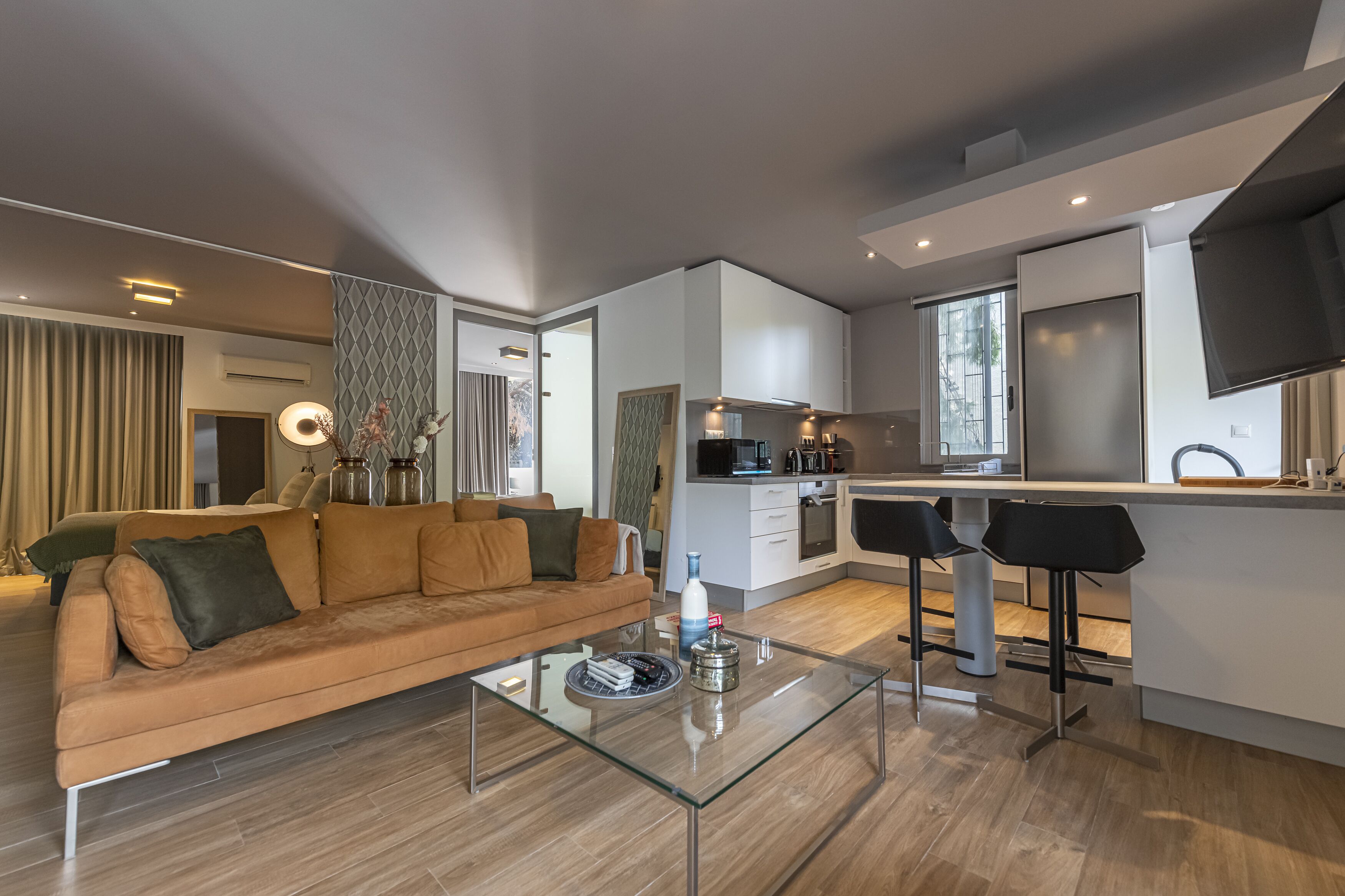 Un salon moderne avec un canapé, une table basse en verre et un coin cuisine doté d’un bar.