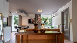 A modern living room with a wooden dining table, two vases with dried plants, a sofa, and a TV mounted on the wall. - Phaedrus Living Luxury Flat Vouliagmeni (Vari-Voula-Vouliagmeni)
