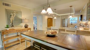Une cuisine spacieuse avec un grand îlot central, des meubles en bois, des luminaires suspendus et un tableau représentant un oiseau.