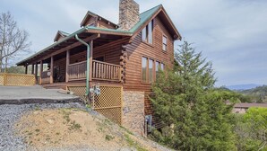 A log cabin with a stone chimney, a porch, and a view of the surrounding landscape. - Ern807 - Black Bearry Ridge - Great Location! Close To All The Action! 6 Bedroom Cabin by RedAwning (Sevierville)