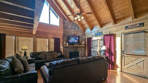 A cabin interior with a stone fireplace, leather sofas, wooden floors, and a television mounted on the wall. - Ern807 - Black Bearry Ridge - Great Location! Close To All The Action! 6 Bedroom Cabin by RedAwning (Sevierville)