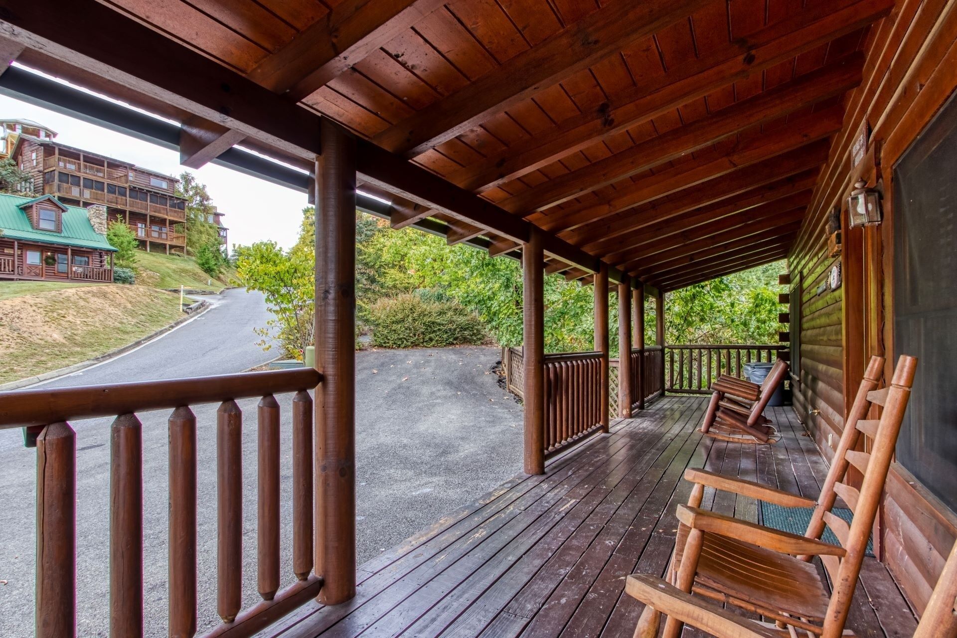 Een houten veranda met een balustrade, houten stoelen en een uitzicht op een weg en gebouwen op de achtergrond.