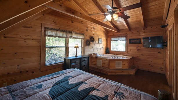 A cozy cabin bedroom with a bed, a vanity, a window, and a ceiling fan. - Ern807 - Black Bearry Ridge - Great Location! Close To All The Action! 6 Bedroom Cabin by RedAwning (Sevierville)