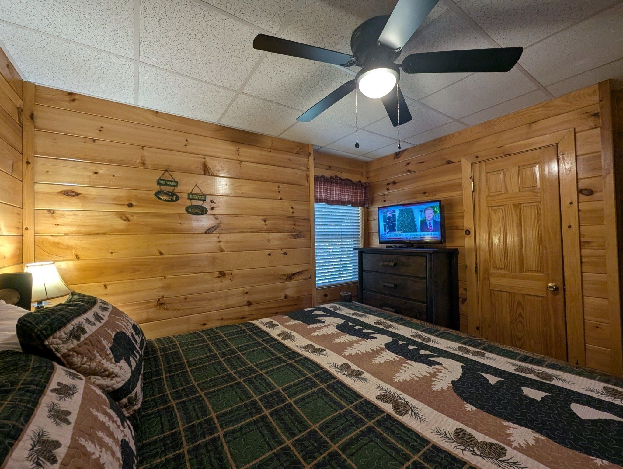 Ein Zimmer in einer Holzhütte mit einem Bett, einem Deckenventilator, einem Fernseher und einem Holzschrank.