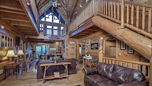 A rustic log cabin interior with a leather couch, wooden tables, and a staircase. - Ern854 - Wagon Wheel Lodge - Great Location! Close To All The Action! 9 Bedroom Cabin by RedAwning (Pigeon Forge)