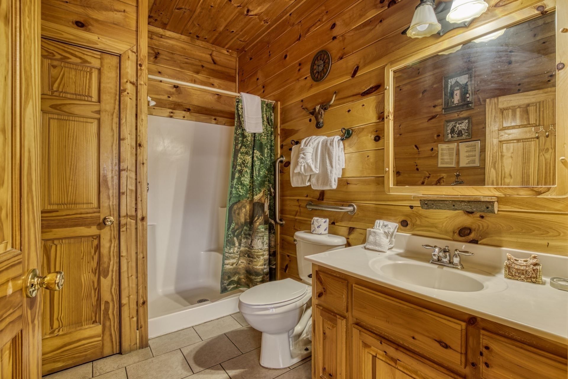 Baño de cabaña de madera con ducha, inodoro, lavabo y un espejo grande.
