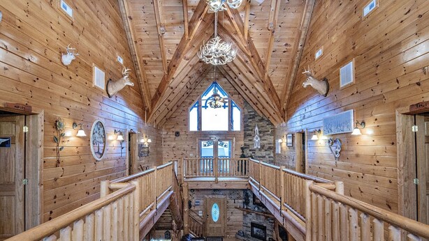 A wooden interior with a central staircase, wooden railings, and a chandelier. - Ern854 - Wagon Wheel Lodge - Great Location! Close To All The Action! 9 Bedroom Cabin by RedAwning (Pigeon Forge)