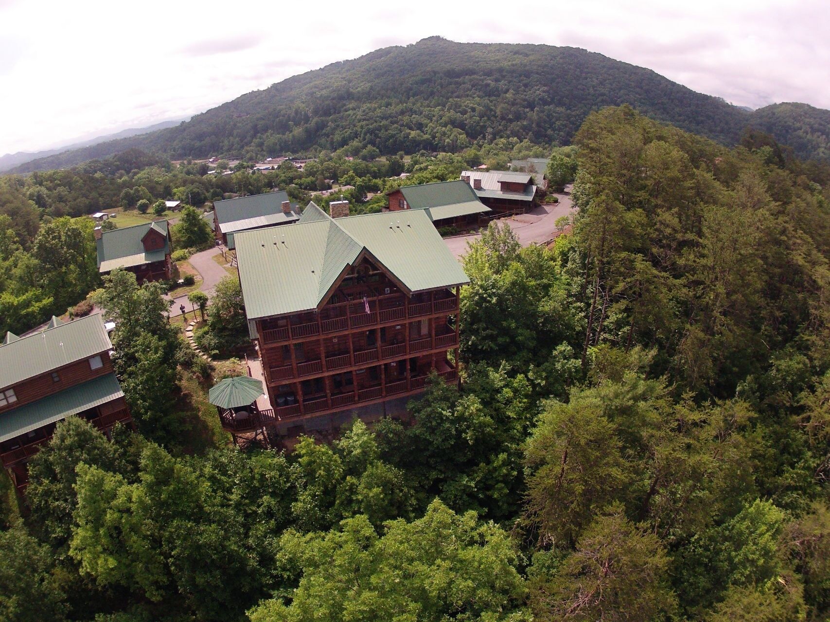 A lodge with a prominent central building surrounded by smaller structures, set in a forested area with a mountain in the background.