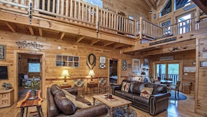A spacious log cabin interior with a high ceiling, wooden floors, and a cozy seating area with leather sofas and a coffee table. - Ern854 - Wagon Wheel Lodge - Great Location! Close To All The Action! 9 Bedroom Cabin by RedAwning (Pigeon Forge)