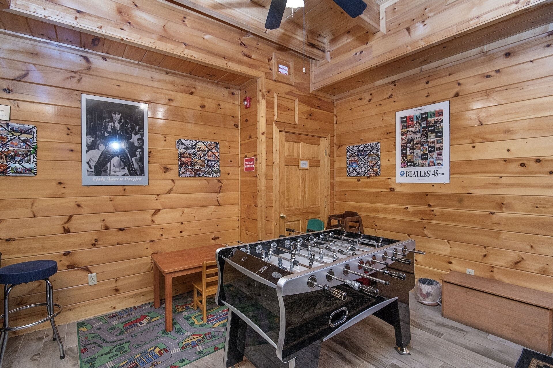 Une pièce chaleureuse aux murs en bois, avec un baby-foot, une petite table et une chaise. Les murs sont ornés de posters et une porte est marquée de l’inscription « Bureaux ».