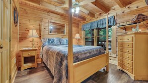 Ein Schlafzimmer einer Holzhütte mit einem Himmelbett, einem Nachttisch, einer Kommode und einem Deckenventilator.