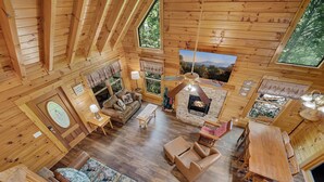 Ein gemütliches Blockhaus-Interieur mit Kamin, Holzmöbeln und großen Fenstern, die einen reizvollen Ausblick bieten.