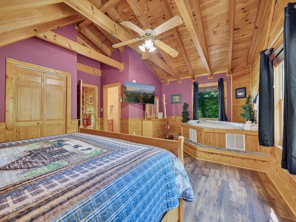 Un dormitorio de cabaña de madera con una cama, ventilador de techo, jacuzzi y un televisor en la pared.