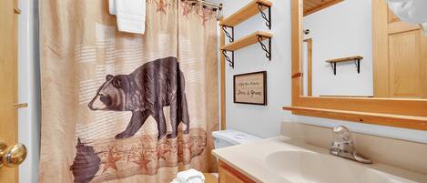 A bathroom with a wooden ceiling, a shower curtain with a bear design, a toilet, a sink, and a mirror.