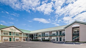 A motel with a green roof and multiple units, a parking lot, and a clear blue sky with clouds. - Colonial Crest 107 - Great Location! - You Can Walk To Town! 1 Bedroom Condo by RedAwning (Pigeon Forge)