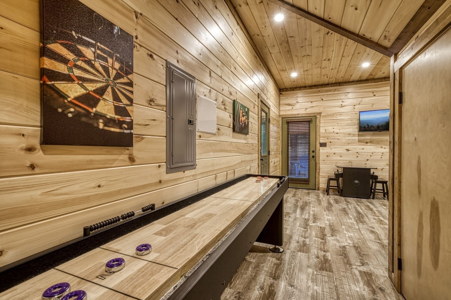 Una habitación con mesa de juego de discos, paredes de madera, dardo y una pantalla de televisión.