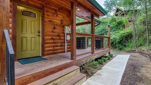 A wooden cabin with a green door, a covered porch, and a concrete pathway leading to the entrance. - Ern841 - Sweet Feet Retreat - Location, Location, And Private Indoor Pool! 2 Bedroom Cabin by RedAwning (Pigeon Forge)