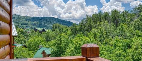 A wooden cabin with a view of a forested mountain and a small house with a green roof.
