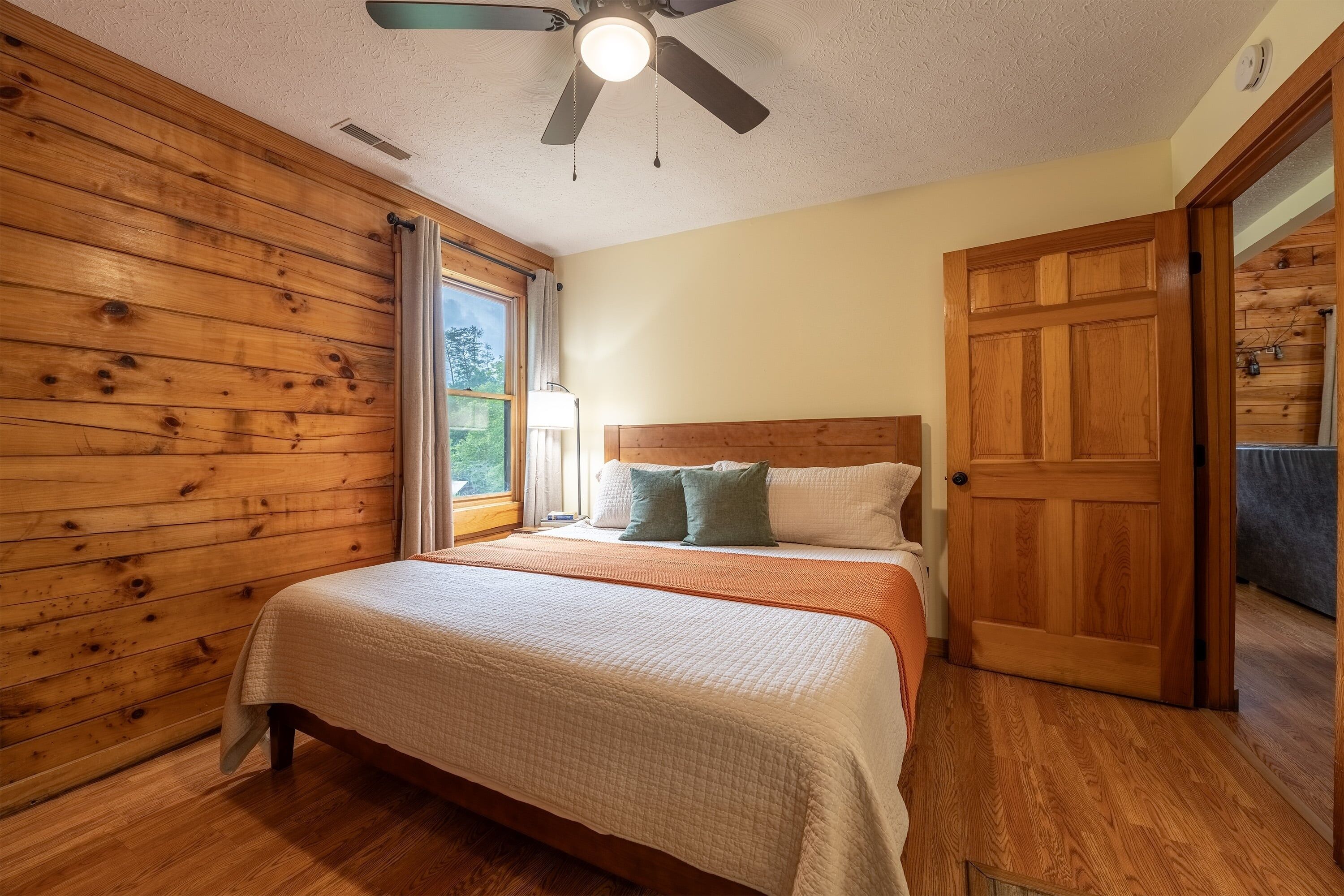 Ein Schlafzimmer mit Deckenventilator aus Holz, einem Bett mit weißer Bettdecke und einer Holztür.