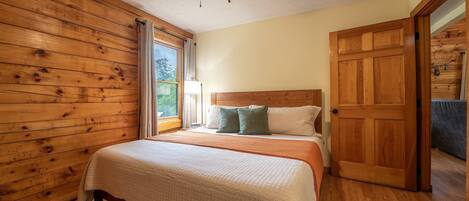 Ein Schlafzimmer mit Deckenventilator aus Holz, einem Bett mit weißer Bettdecke und einer Holztür.
