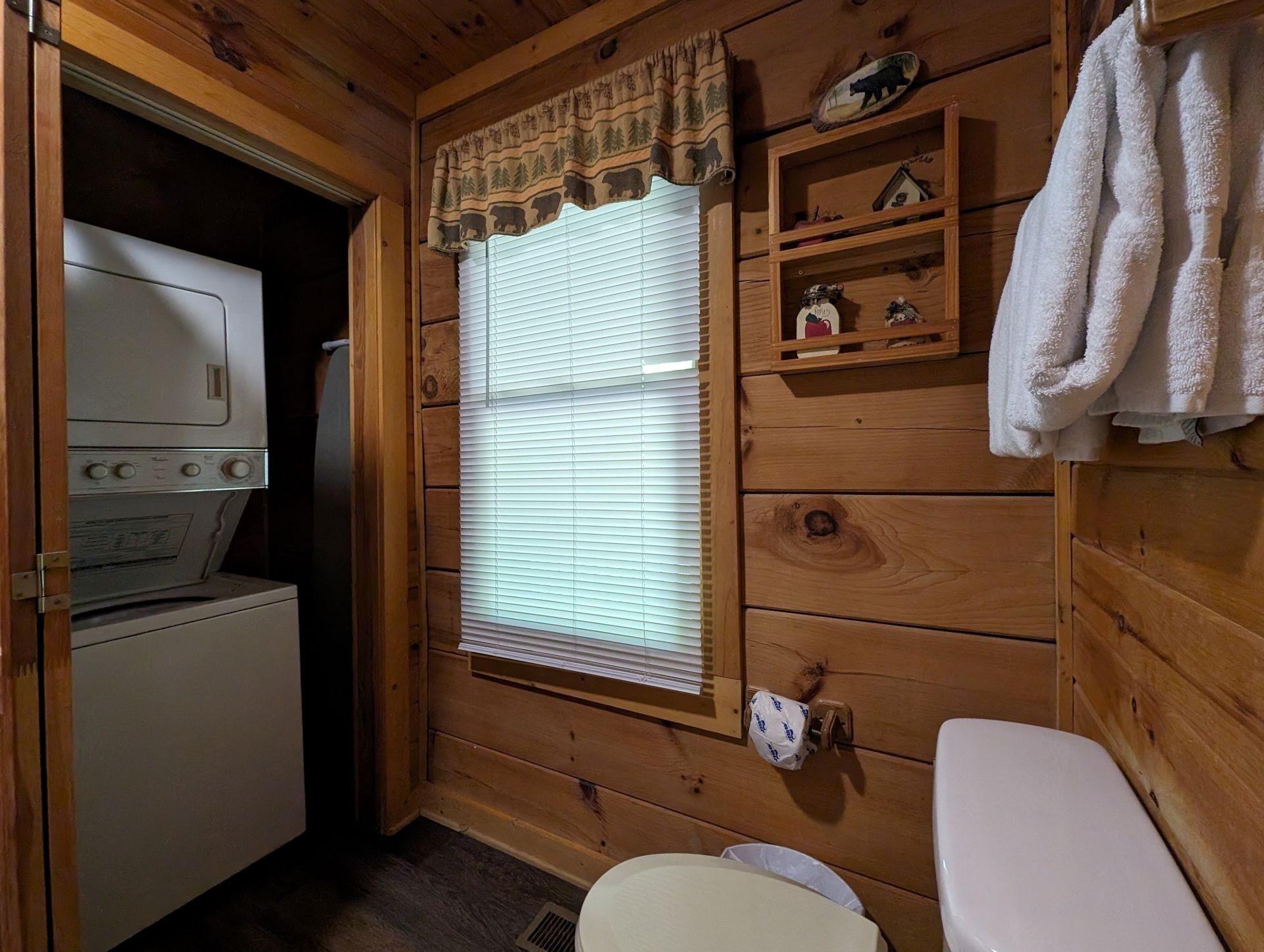 A compact wooden cabin bathroom with a washing machine, toilet, and a shelf with towels.