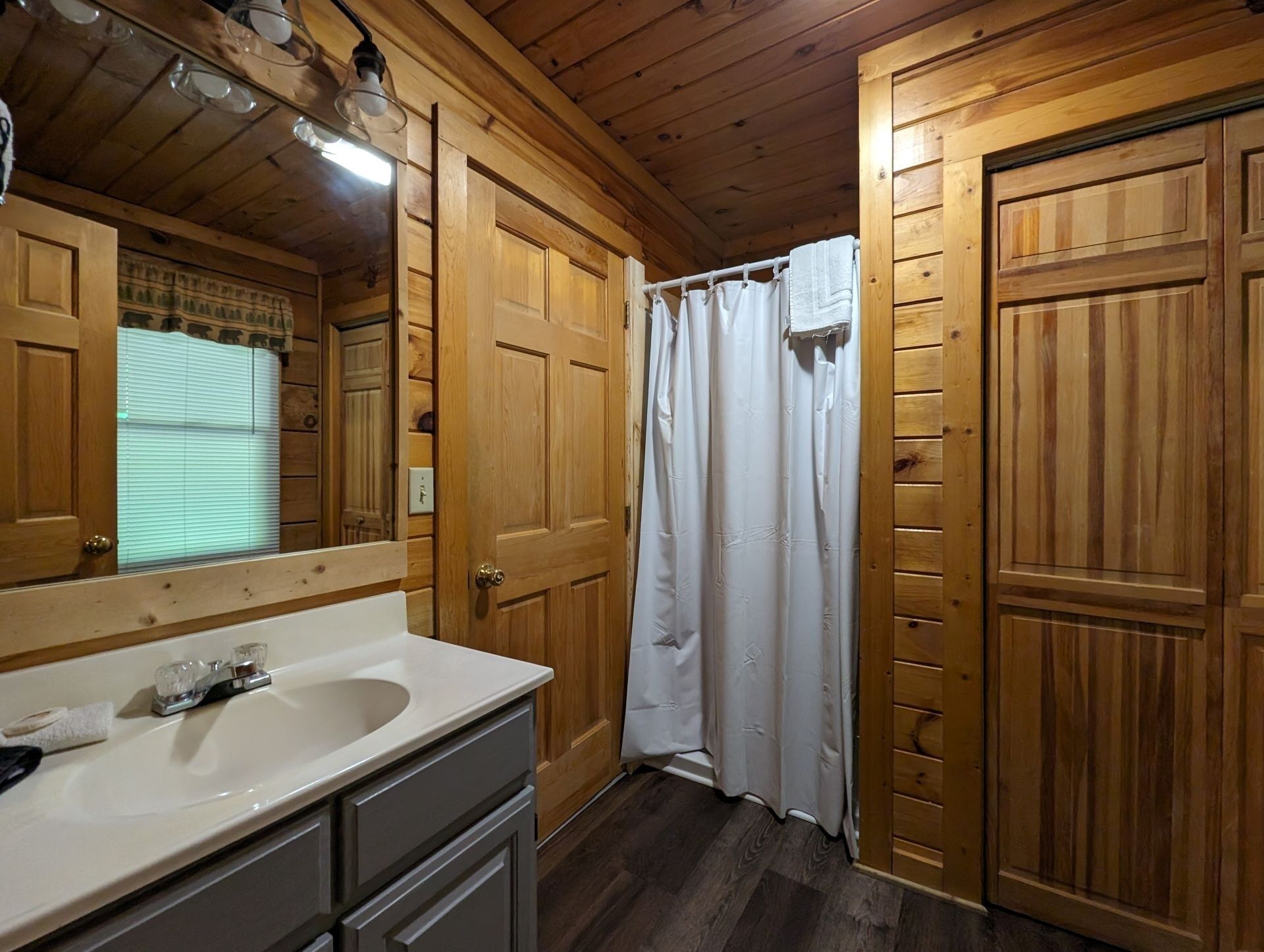 Bagno di una casetta in legno, con lavandino, specchio e tenda da doccia.