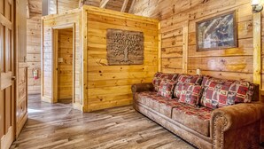 A wooden cabin interior with a sofa and a framed picture of deer.