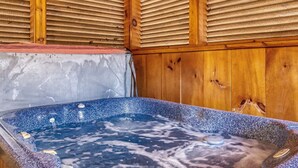 A hot tub with a wooden interior, a stone wall, and a wooden ceiling with slats.