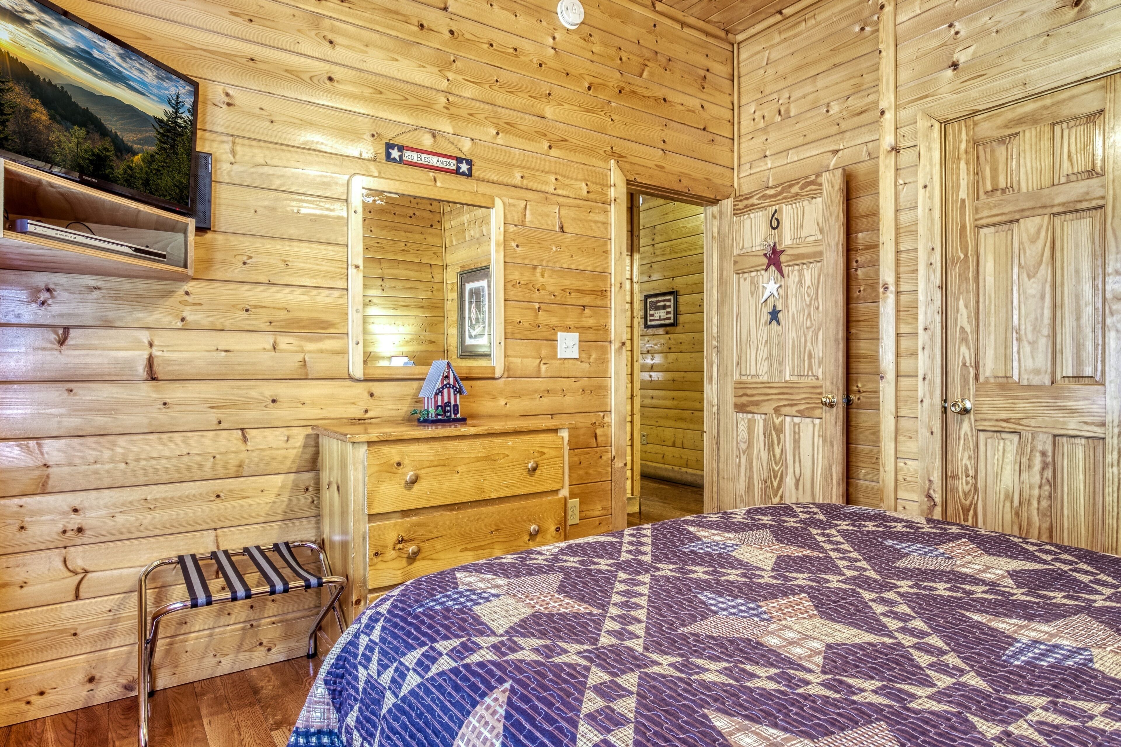 Ein Holzblockhaus-Zimmer mit Bett, Kommode und an der Wand befestigtem Fernseher.