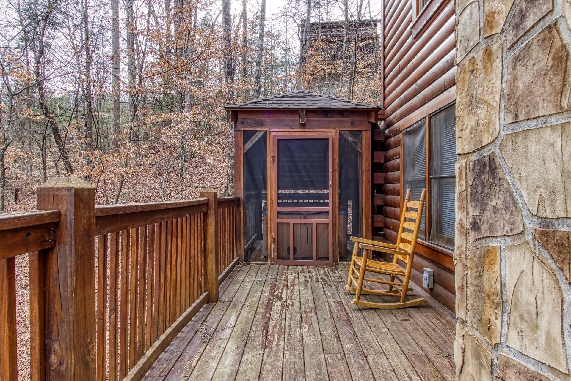 Une terrasse en bois avec une chaise berçante, un petit abri en bois et un mur en pierre.