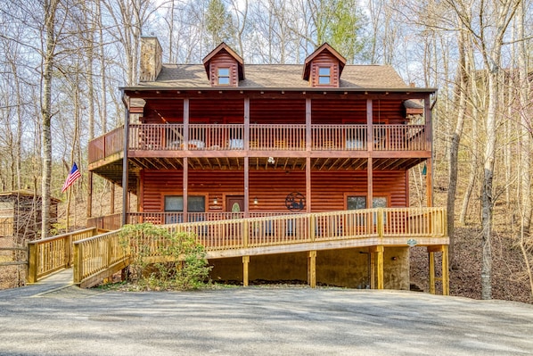A two-story log cabin with a balcony, a flag, and a wooden deck.