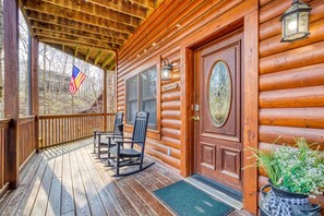 Een houten hut met een veranda, schommelstoelen, een deur met ruit en een vlag.
