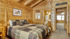 A wooden cabin bedroom with a bed, a framed baseball bat and glove, a wooden ceiling, and a door leading to a bathroom. - Er305- Bear Right Inn- Great Location- Close To Town 9 Bedroom Cabin by RedAwning (Pigeon Forge)