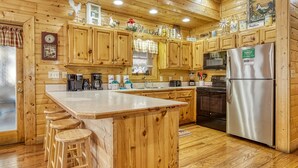 A wooden cabin-style kitchen with a central island, bar stools, a stainless steel refrigerator, and wooden cabinets. - Er305- Bear Right Inn- Great Location- Close To Town 9 Bedroom Cabin by RedAwning (Pigeon Forge)