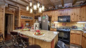 A wooden kitchen with a granite countertop, a refrigerator, a microwave, a stove, and hanging light fixtures. - Liam's Retreat - 2 Bedroom with GameRoom just minutes away from Pigeon Forge 2 Cabin by RedAwning (Sevierville)