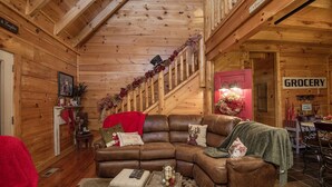 A cozy log cabin interior with a wooden staircase, a sectional sofa, and a visible grocery sign. - Liam's Retreat - 2 Bedroom with GameRoom just minutes away from Pigeon Forge 2 Cabin by RedAwning (Sevierville)