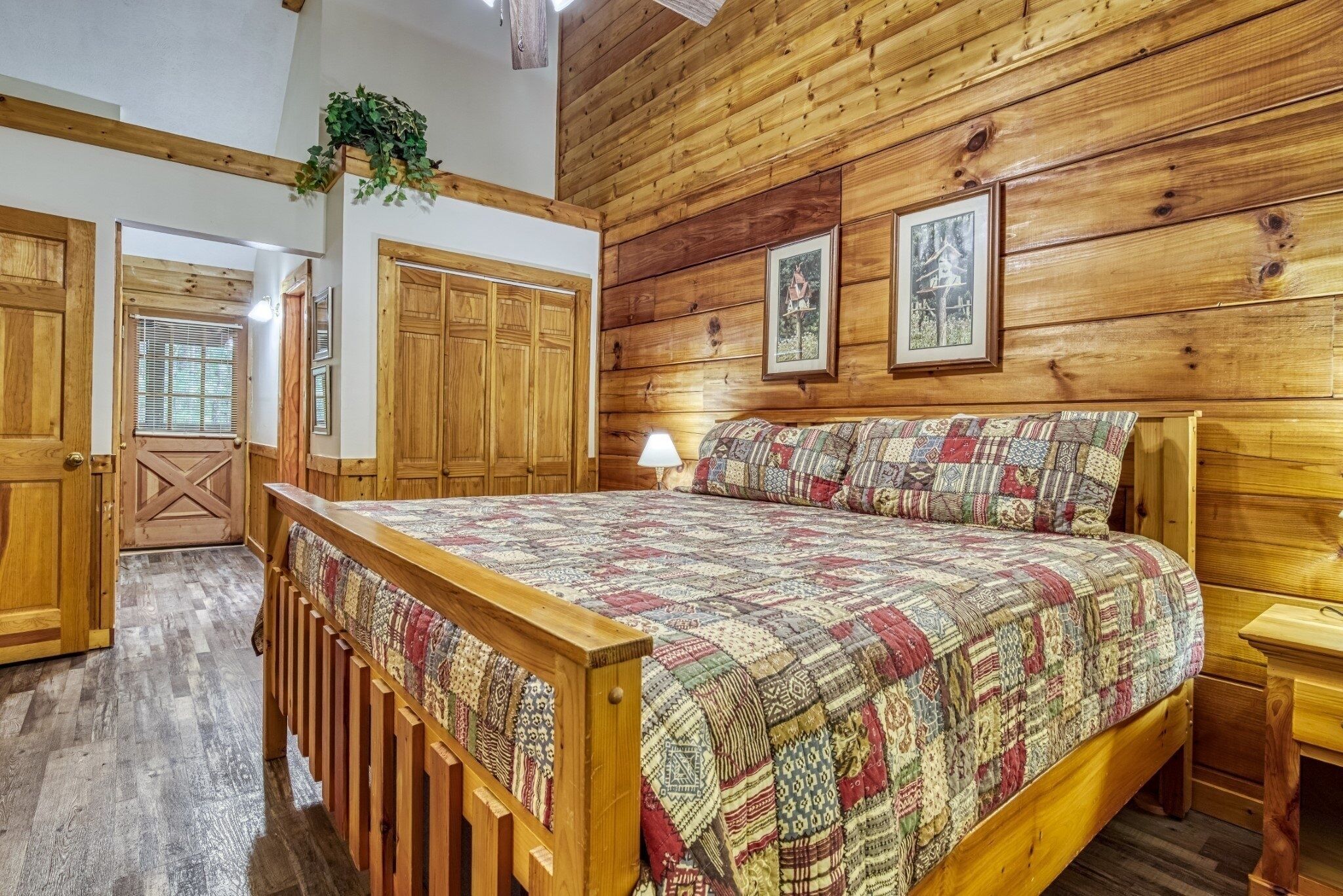 Une chambre aux murs lambrissés, avec un grand lit, une armoire en bois et une fenêtre équipée de stores.
