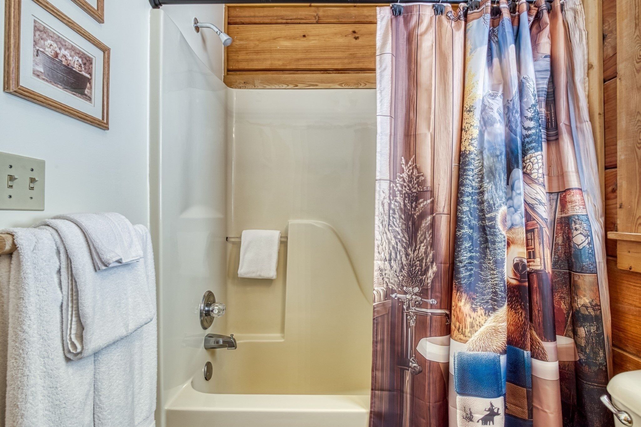 A bathroom with a bathtub, a shower curtain with a forest and wildlife design, and a towel hanging on the wall.