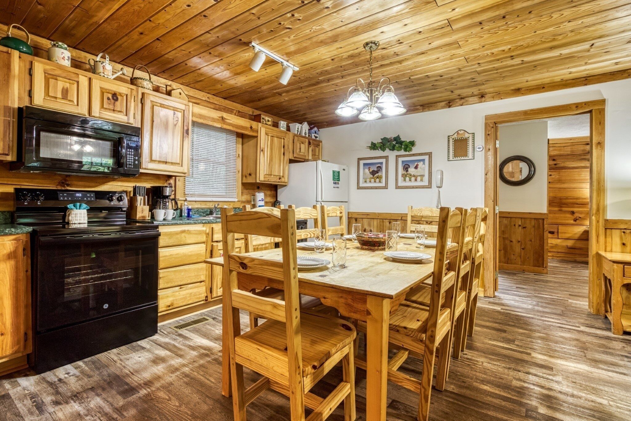 A wooden cabin-style kitchen with a dining area, featuring wooden cabinets, a microwave, a stove, and a dining table set for four.