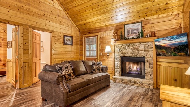 A cozy log cabin interior with a stone fireplace, wooden walls, and a leather sofa. - Er 229 Brief Escape - Great Location Close to Town - 4 BR Cabin by RedAwning (Pigeon Forge)