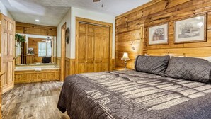 A bedroom with a wooden headboard, a large bed with a quilted cover, a wooden floor, a wooden door, and a ceiling fan. - Er 229 Brief Escape - Great Location Close to Town - 4 BR Cabin by RedAwning (Pigeon Forge)