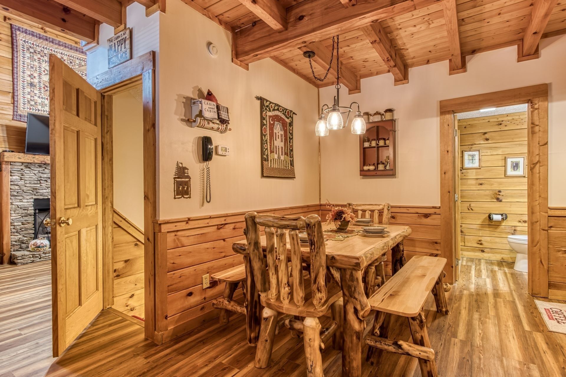A rustic wooden dining area with a wooden bench and table, a stone fireplace, and a wooden ceiling.
