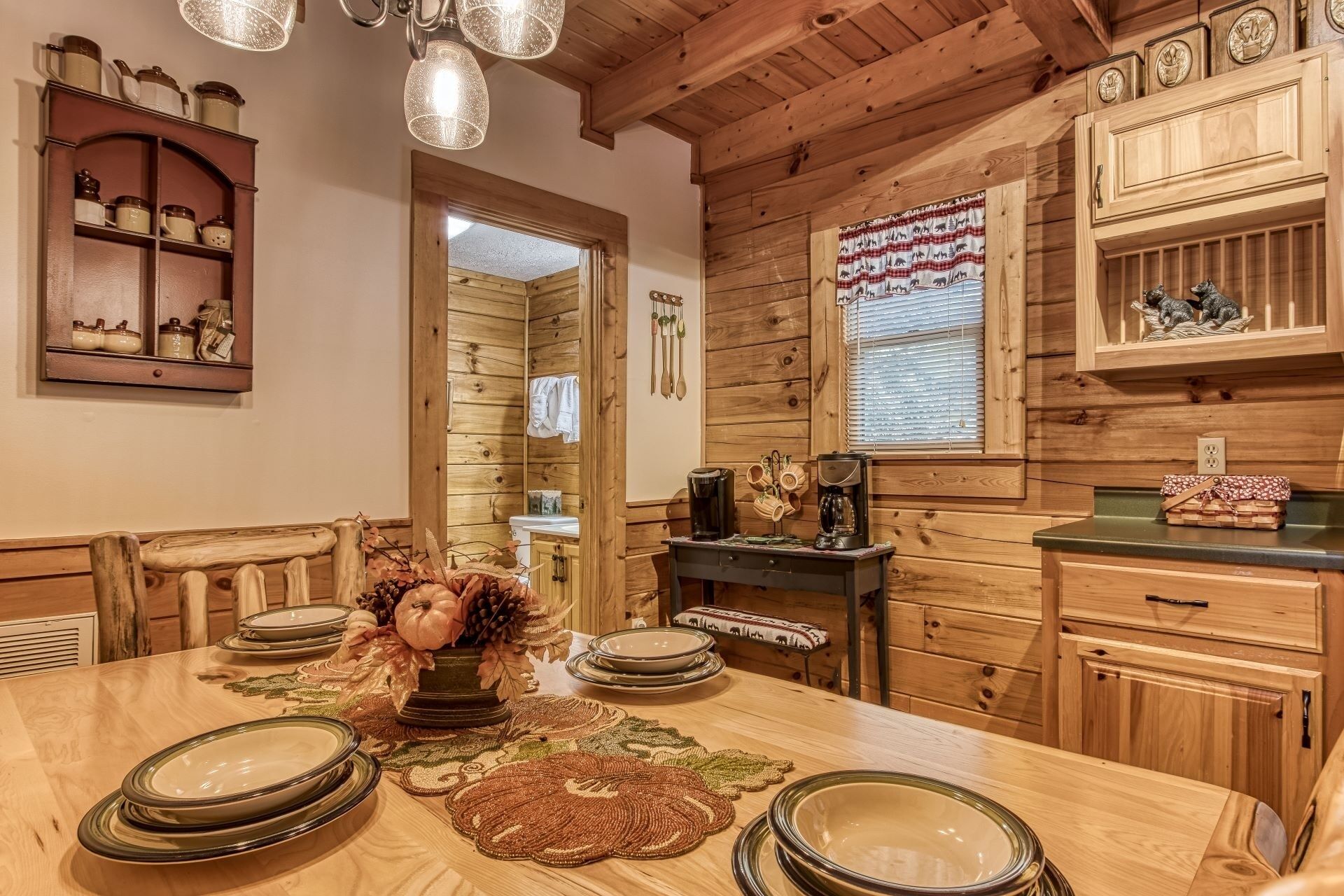 Un comedor de madera con una mesa dispuesta para cuatro personas, una cafetera y un centro de mesa decorativo.