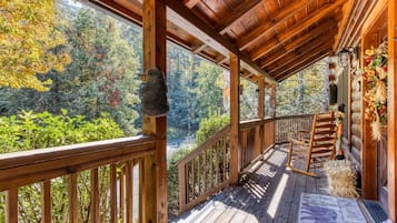Una terraza de madera con barandilla, una mecedora y vistas a zona boscosa.