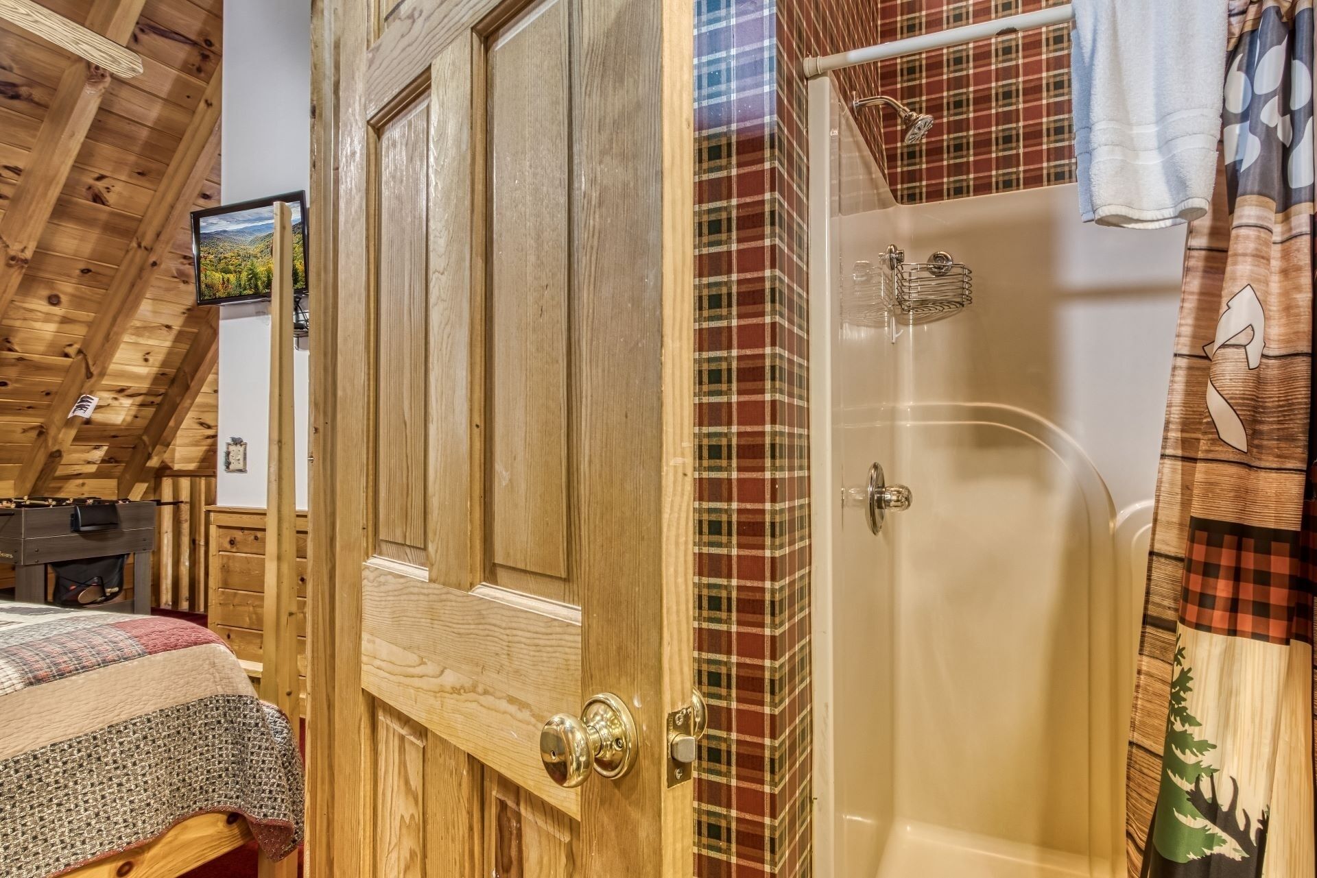 A wooden door with a brass handle, a shower with a glass door, and a plaid-patterned wall.