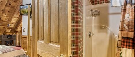 A wooden door with a brass handle, a shower with a glass door, and a plaid-patterned wall.