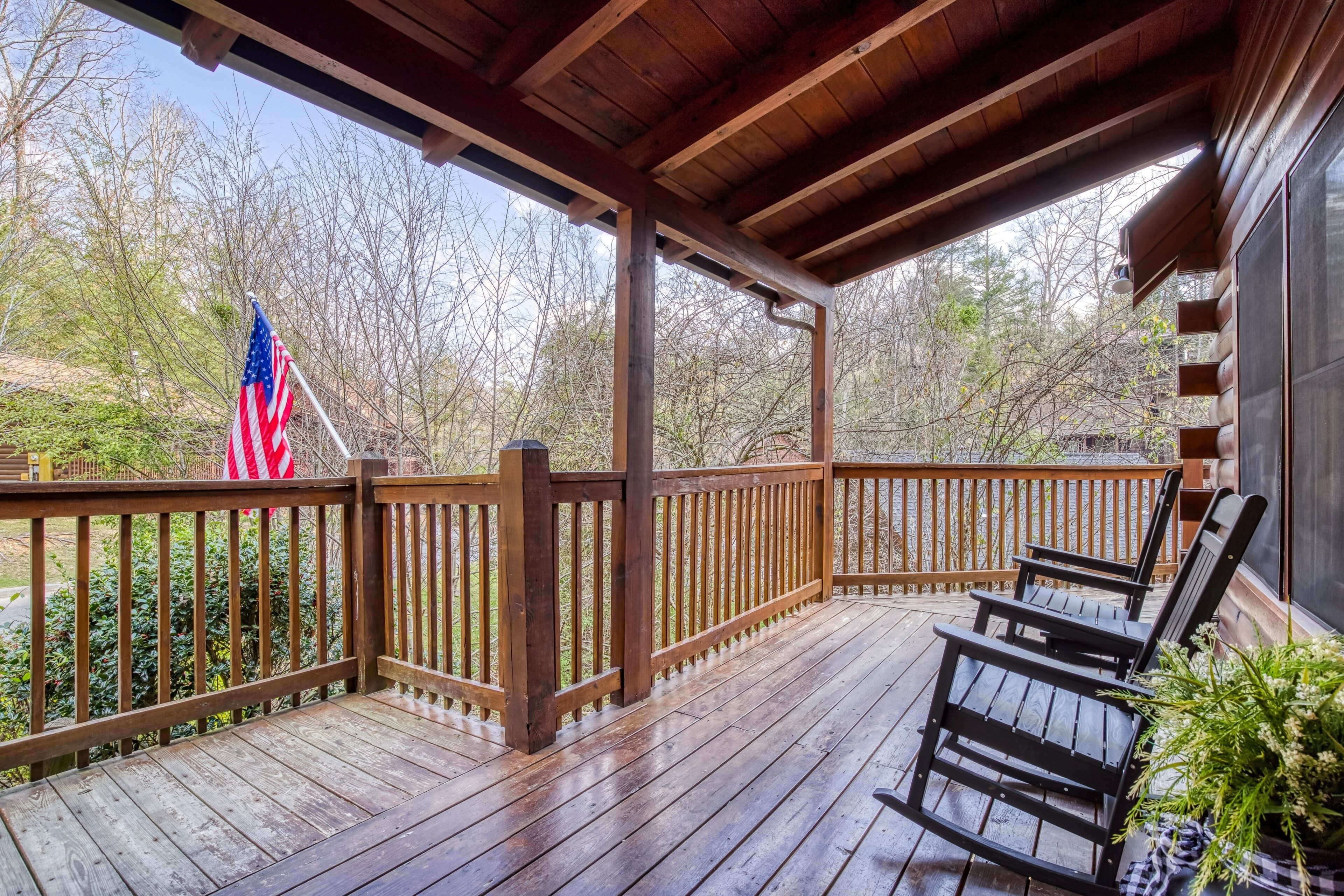 A wooden deck with a railing, two chairs, and an American flag.